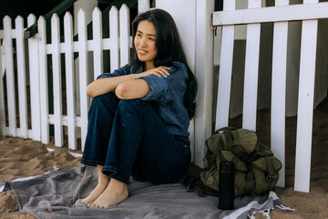 Chinese woman relaxing on a sandy beach near a white picket fence in the sunshine