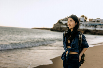 Chinese woman enjoying a peaceful walk along the sandy beach during sunset with gentle waves in the...