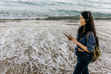 Chinese woman walks along the beach listening to music on a sunny day while checking her phone