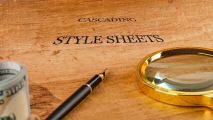 A wooden surface holds a pen and a magnifying glass alongside a rolled-up currency note,...