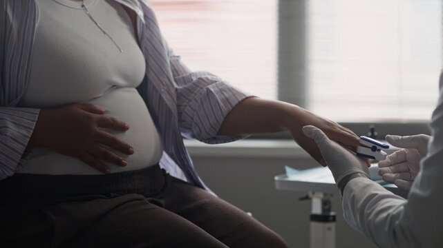 Tilt up of African American male physician checking pregnant woman blood glucose levels using handheld device to screen for gestational diabetes during routine prenatal appointment