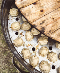 A large metal bowl with a wooden board on top of it. The bowl is filled with dumplings
