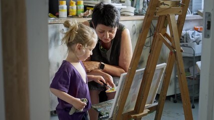 Child painting with an grandmother in a cozy art studio. Candid indoor moment of creativity and learning. Artistic lifestyle scene with real people and natural light.