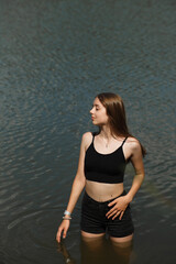 Girl in black shorts stands knee-deep in water in a lake