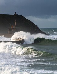 Coastal waves crash against a hill with a lighthouse