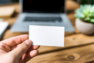 Hand holding blank business card mockup in cozy workspace with notebook. White card template against marble table background. Perfect for branding presentation.