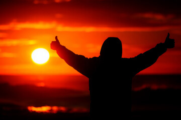 Silhouette of person standing in ocean with outstretched arms at vibrant sunset.