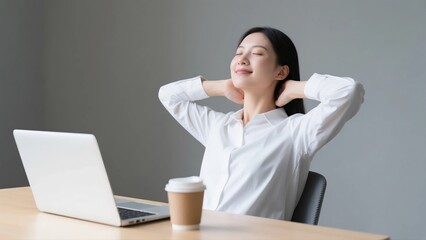 A peaceful young Asian businesswoman relaxing and stretching her arms behind her head with eyes closed while taking a break from work at her desk.