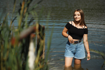 Girl in blue shorts in summer in nature near a small pond
