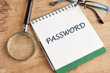 On a wooden desk, a notepad titled PASSWORD sits alongside a magnifying glass and reading glasses,...