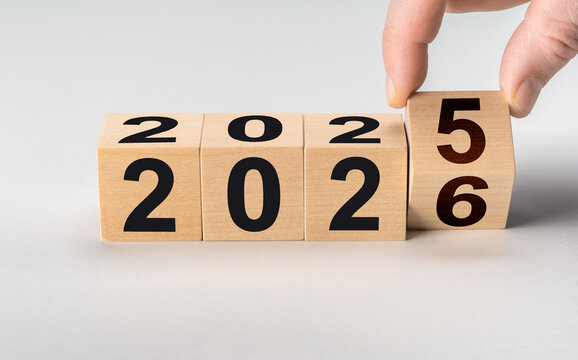 Fingers flipping wooden block to change date from 2025 to 2026. New year's eve and fresh start business concept