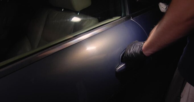 A car thief in black gloves pulls the car door handle at night, trying to rob or steal a car.Concept for advertising the installation of alarm systems or guarded parking