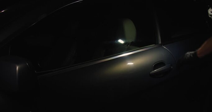 A car thief in black gloves pulls the car door handle at night, trying to rob or steal a car.Concept for advertising the installation of alarm systems or guarded parking