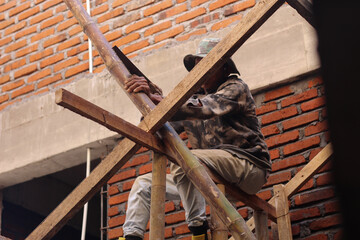 Asian Worker Sawing Bamboo with Traditional Saw While Sitting on Wooden Scaffold