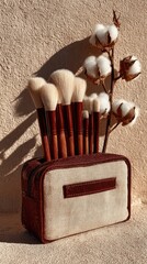 Makeup brushes in a cream-colored, leather-trimmed pouch, beside cotton bolls