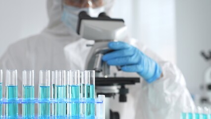A medical virologist in protective gear and blue gloves examines viral samples under a microscope...