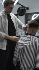Professional barber carefully trimming customer's hair with electric clipper, providing a stylish...