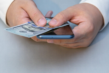 Male hands holding phone and hundred dollars. Online business, rising mobile communication costs, price of mobile network and mobile internet