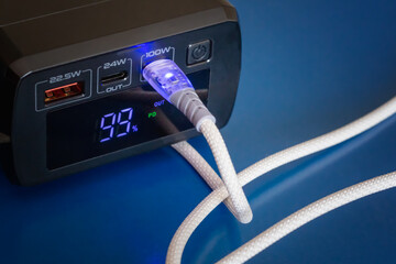 Power bank with percentage numbers on display and white cable in port showing 10 watts close-up blue background, autonomous power,