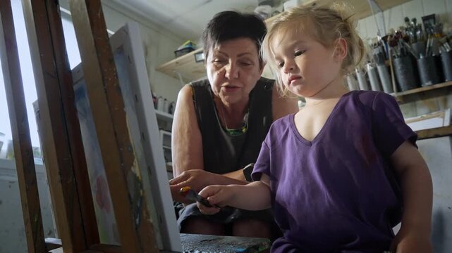 Child painting with an grandmother in a cozy art studio. Candid indoor moment of creativity and learning. Artistic lifestyle scene with real people and natural light.