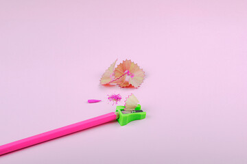Sharpening pink pencil with green sharpener and shavings, on pink pastel backround.