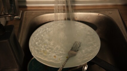 Water runs onto dirty plate and fork in sink after faucet turns on