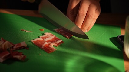 Hands slicing bacon strips on green cutting board in kitchen