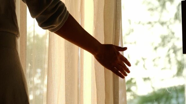 woman's hand She opened the curtains on the window. There was morning light through the window in her room, looking at the view of the mountains and trees as the sun rose	