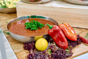 A Vibrant Display of Fresh Ingredients Featuring a Bowl of Rich Sauce Accompanied by Colorful Peppers and Green Garnish on a Wooden Board