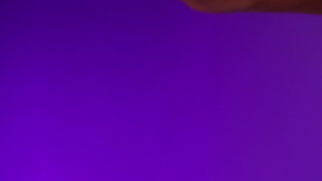 Extreme close-up female hamd  holding  sealed condom   on a lilac background