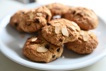 Close-up of homemade almond and raisin cookies on a white plate. Freshly baked rustic cookies topped with sliced almonds, perfect for a sweet treat or snack.