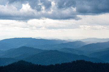 Fototapeta premium Layers of blue mountains recede into the distance under a cloudy sky, creating a sense of depth and serenity