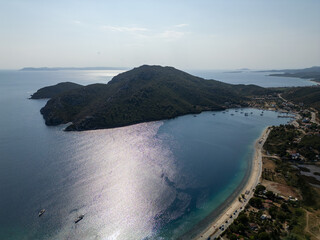 Aerial view of a peaceful bay with anchored sailboats and lush green hills. The calm sea reflects...