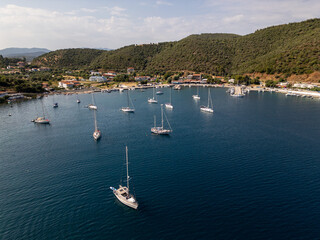 Aerial view of a marina with multiple sailboats anchored near a coastal village surrounded by green...