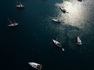 Aerial top-down view of several sailboats anchored in calm dark blue sea water with sun...
