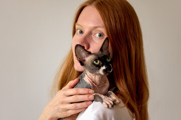 Woman holding a Sphynx cat against a soft neutral background