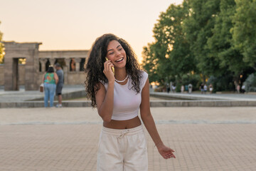 Young woman laughing while talking on phone in front of the temple of debod, madrid