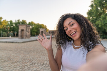 Tourist taking selfie and waving in madrid park with temple of debod