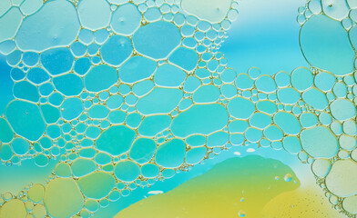 Vibrant macro shot of oil bubbles on colorful blue and yellow liquid surface, forming organic...