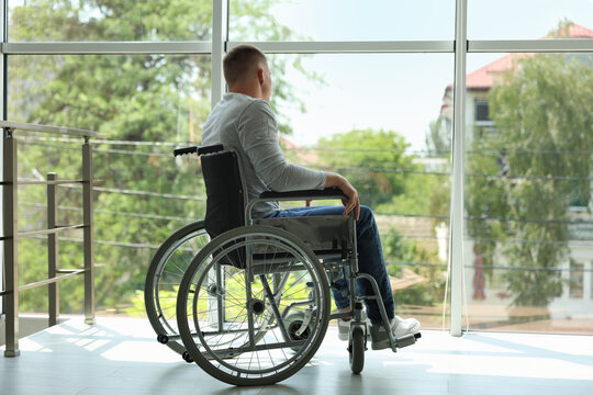 Young man in wheelchair near window indoors