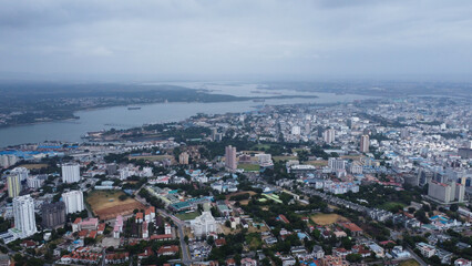 Extensive aerial view of a sprawling city with dense buildings and a large bay under cloudy sky.