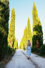 Dreamy Tuscan landscape with cypress road and female traveler enjoying nature.