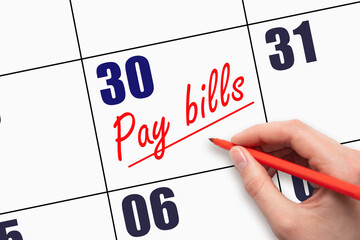 30th day of the month.  Hand writing Pay bills reminder and drawing a line on calendar with red pen...