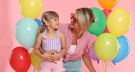 Obraz premium Happy mother in sunglasses and her little daughter with bunches of colorful balloons on pink background