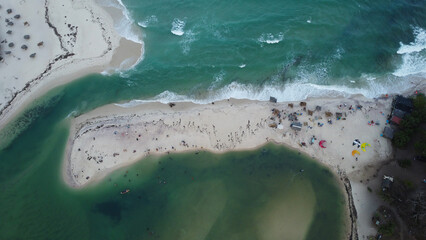 Aerial View of Tropical Beach: Turquoise Ocean Waters Meet Sandy Shoreline with People Relaxing.