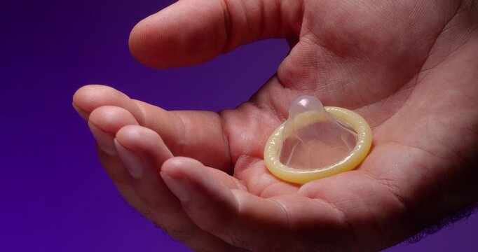 Super close-up of a male palm holding an unused condom on a lilac background