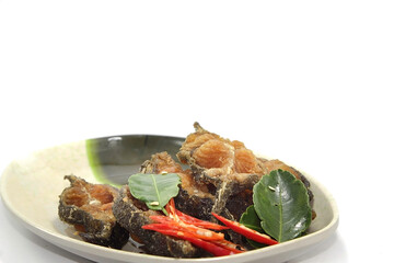 Traditional fried catfish garnished with kaffir lime leaves and red chili on a plate. On a white backdrop
