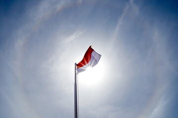 The red and white flag fluttering high fluttered in the wind in the air against the backdrop of a cloudy blue sky