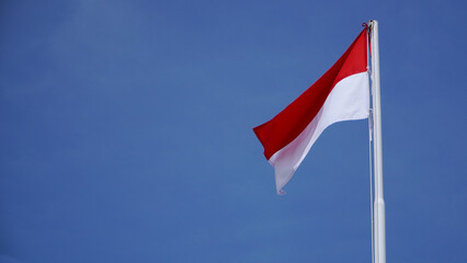 The red and white flag fluttering high fluttered in the wind in the air against the backdrop of a cloudy blue sky
