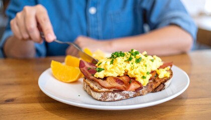 A person enjoys a delicious breakfast of scrambled eggs, bacon, and orange slices